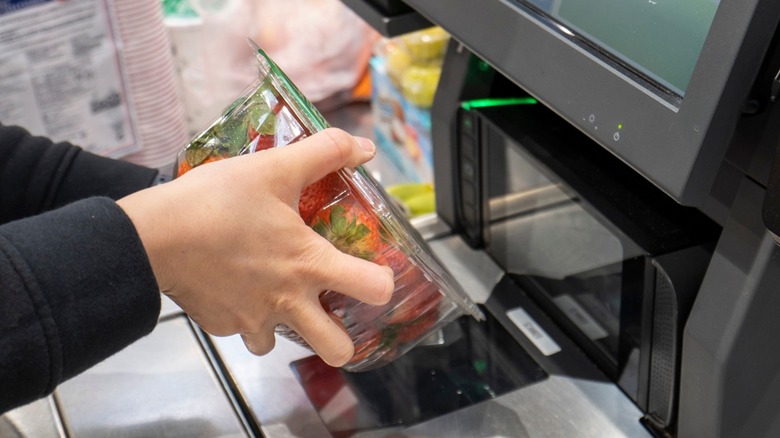 Person scanning barcode on container of strawberries in supermarket