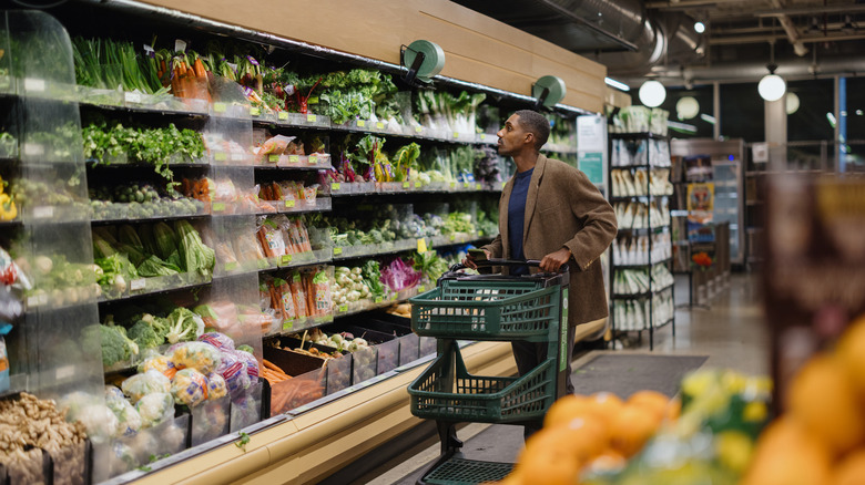 A man with a grocery cart looking at the produce in a grocery store