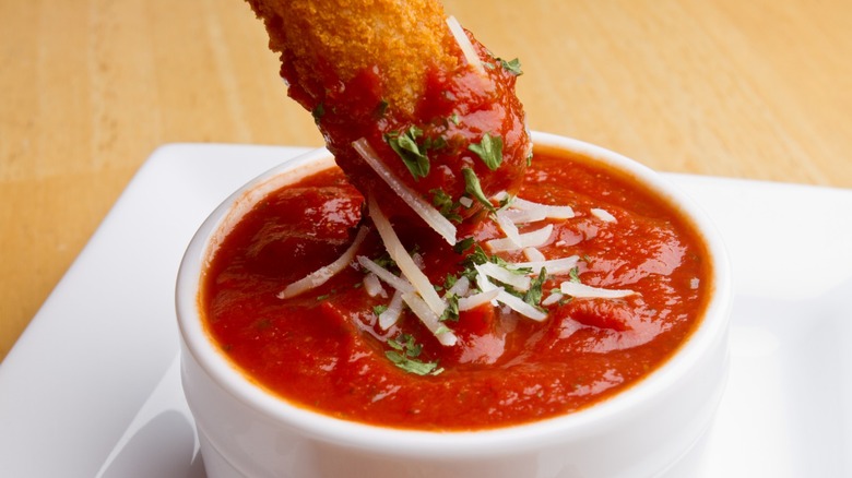 A mozzarella stick being dipped into a cup of marinara sauce.