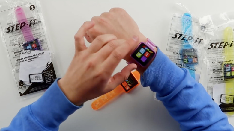 Reviewer's hands demonstrating the purple and orange versions of the Step-It fitness tracker from McDonald's.