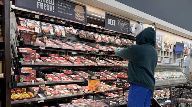 A person in a hoodie shopping for beef in the meat section of a grocery store