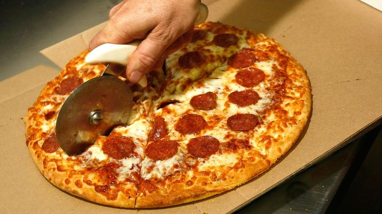 A hand cutting a Little Caesars pizza on a cardboard box