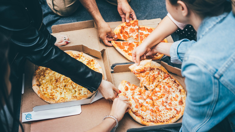 A group of friends taking slices of various pizzas out of boxes