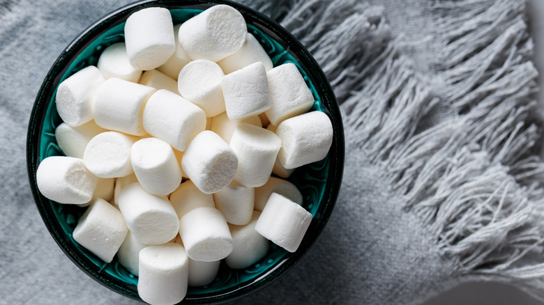 Top view of white marshmallows in a bowl on top of gray fabric.