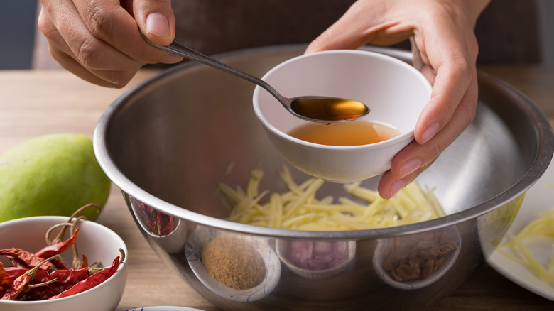 fish sauce being spooned into bowl of papaya salad