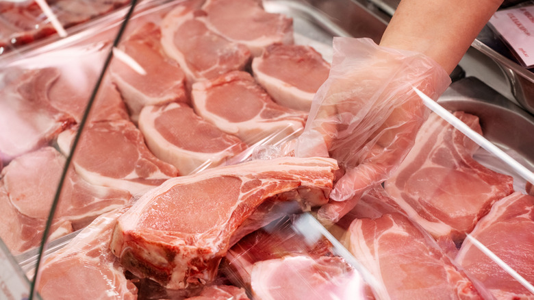 A butcher selects a pork chop from a display case