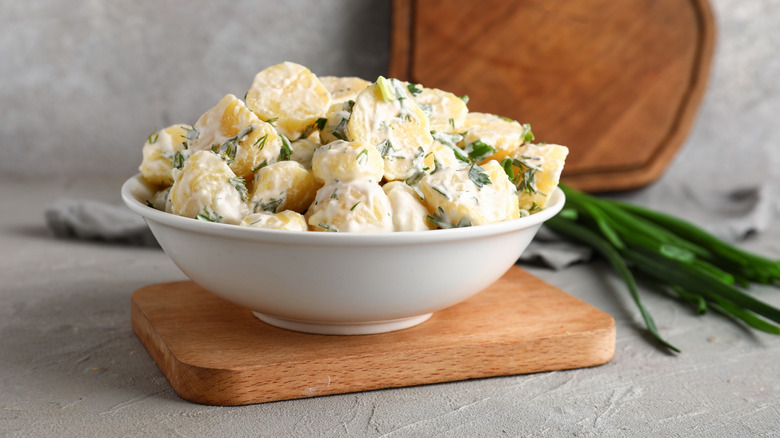 A creamy potato salad with herbs served in white bowl.