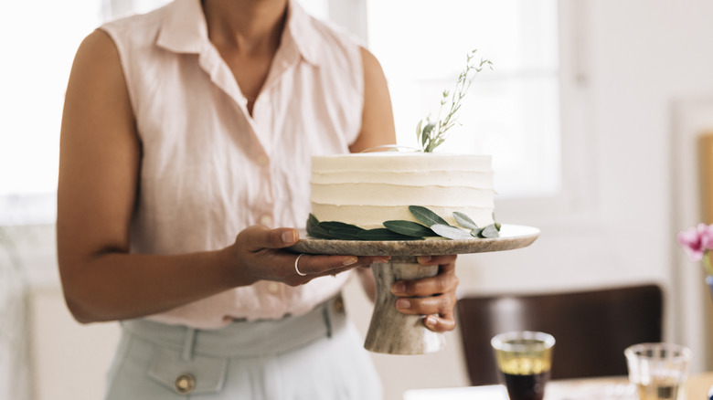 A woman carrying an iced, decorated cake on a stand