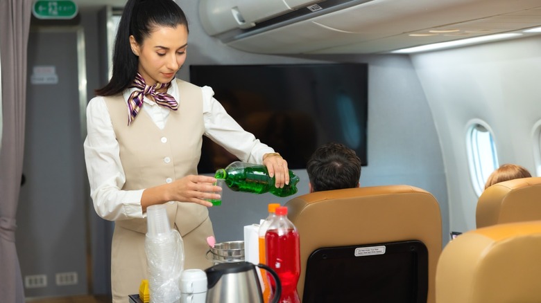 A flight attendant serving drinks from a cart.