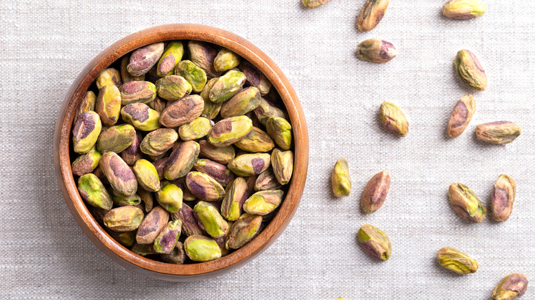 A ramekin of shelled pistachios on a fabric background.