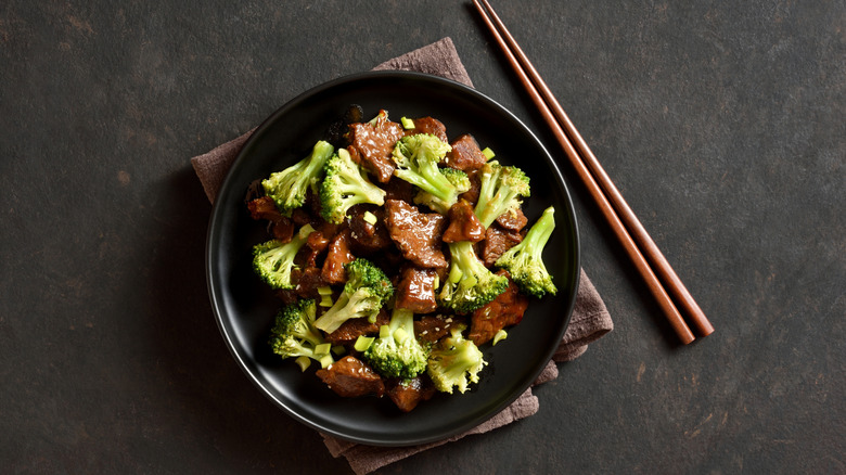 Black bowl of beef and broccoli next to chopsticks