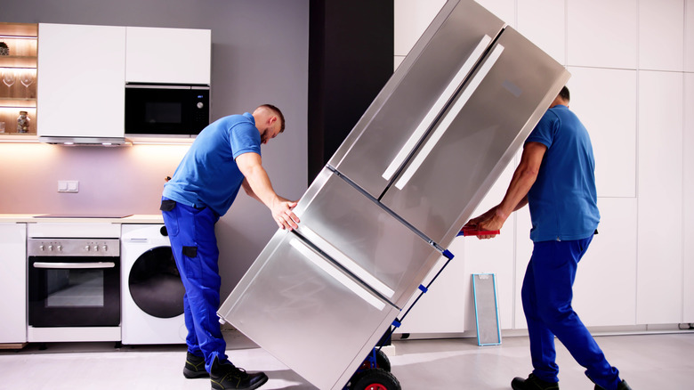 Two men in blue uniforms deliver silver fridge