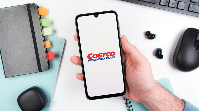 Hand holds phone open to Costco app at desk