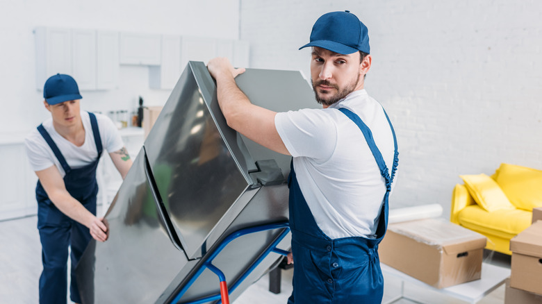 Two men move fridge through home on appliance dolly
