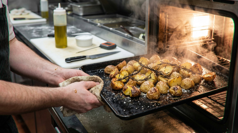 person removing steaming potatoes from an oven