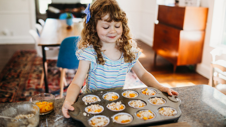 Young girl picking up a muffin tray