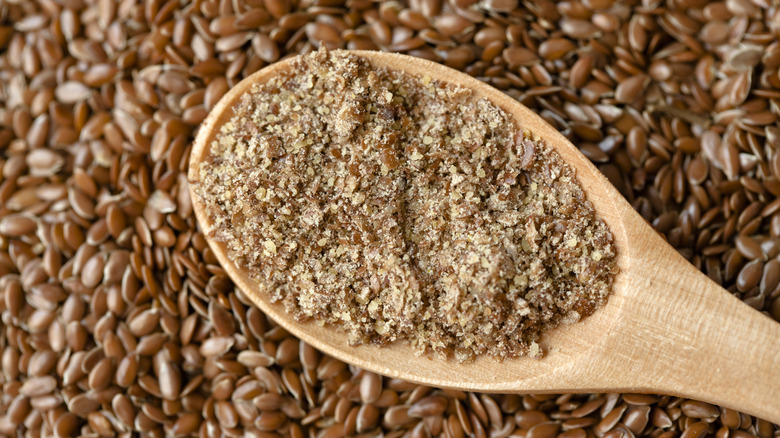 Wooden spoon with ground brown flaxseed inside and whole brown flaxseeds in the background