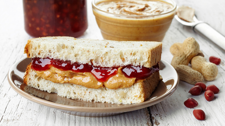 Half a peanut butter jelly sandwich with peanut butter and jelly in background