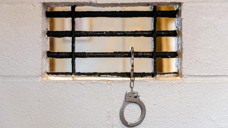 handcuffs hang from a small barred window in a cinderblock wall