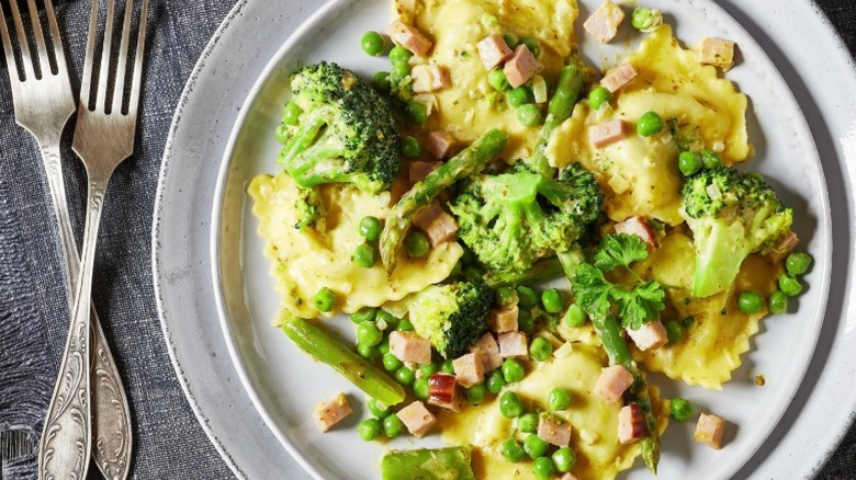 Plate of ravioli with broccoli, asparagus, peas, and ham.