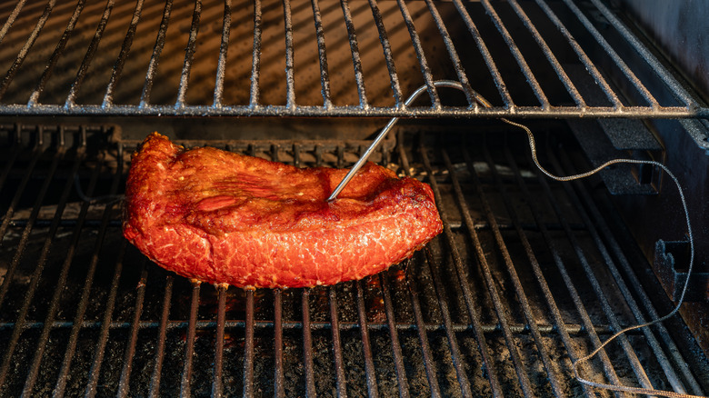 probe thermometer stuck in a brisket that's still inside a smoker