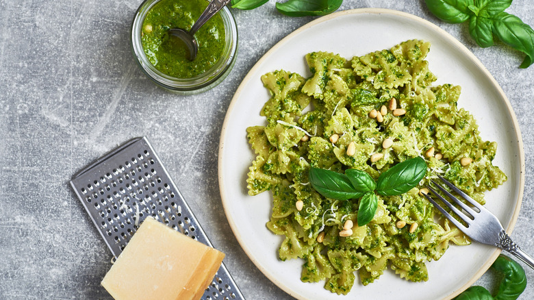 A bowl of pasta with pesto sauce, with basil and parmesan cheese around it on the table