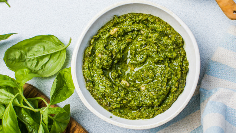 A bowl of pesto sauce with fresh basil leaves next to it