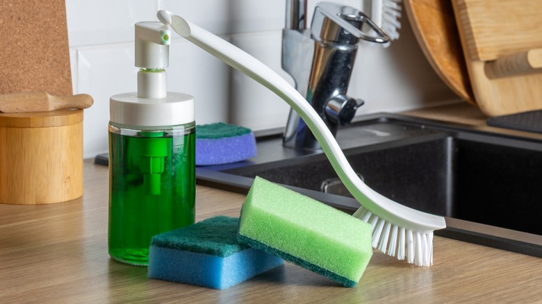 A clean kitchen counter with a green soap dispenser, sponges, and brush