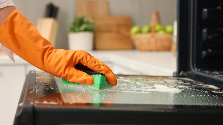 Person with gloved hand cleaning oven with sponge