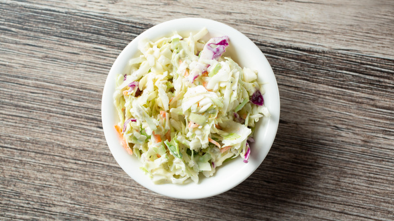 A small white bowl full of coleslaw on a gray wooden table
