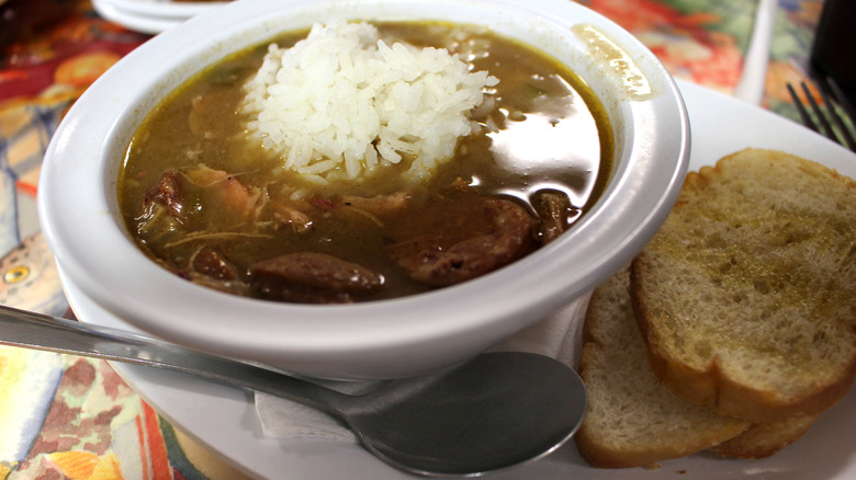 Gumbo in white bowl with bread and a spoon