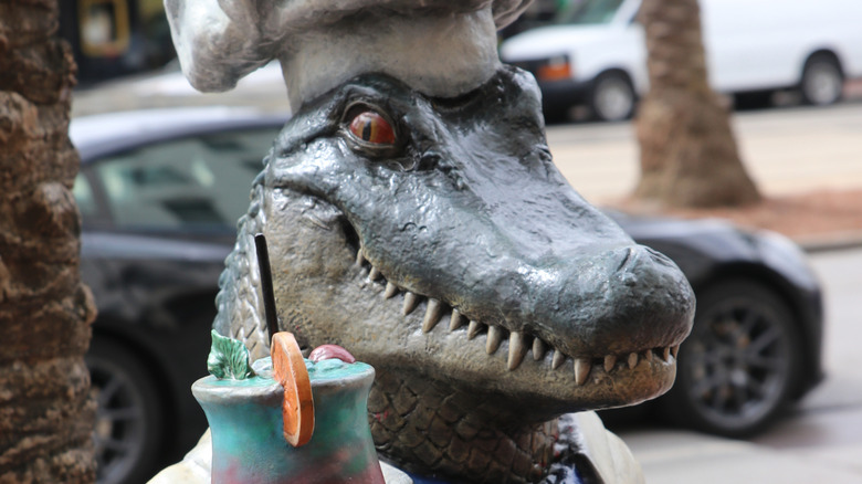 statue of an alligator in a chefs hat holding a drink