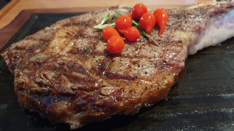 Browned cooked tomahawk steak topped with several grape tomatoes and a couple of small rosemary springs on a black surface