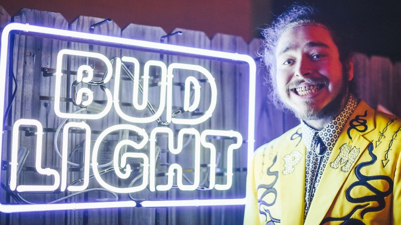 Singer Post Malone stands next to a Bud Light neon sign