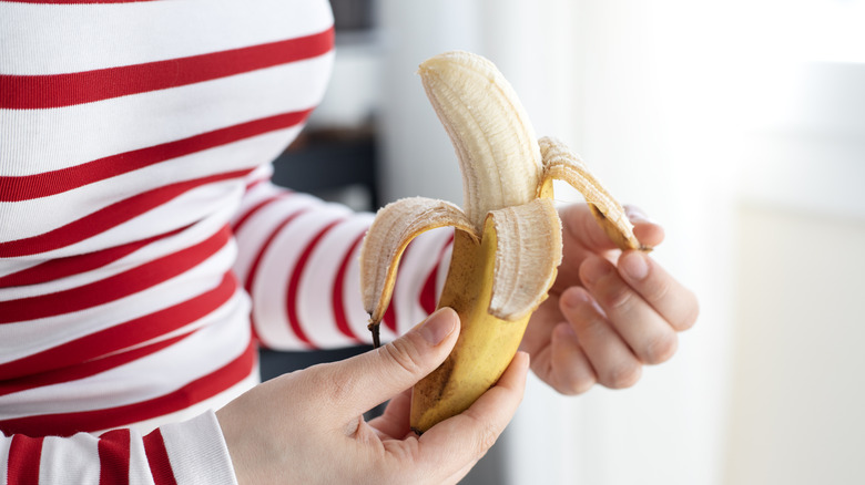 A woman holding a peeled banana in her hands