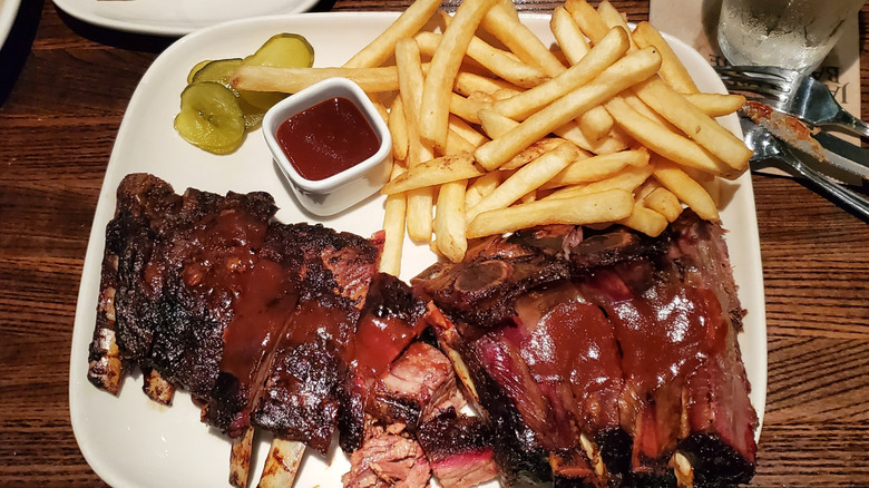 A plate of Kansas City-style BBQ ribs, french fries, and pickles with extra sauce.