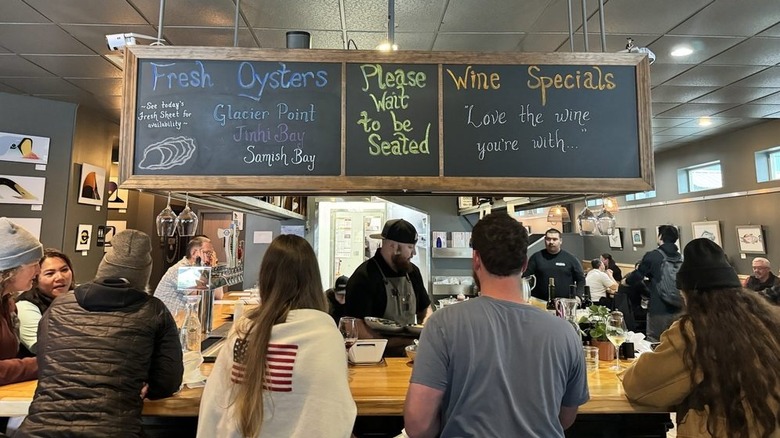 A view of the backs of people sitting at bar with chalkboard sign above at The Cookery