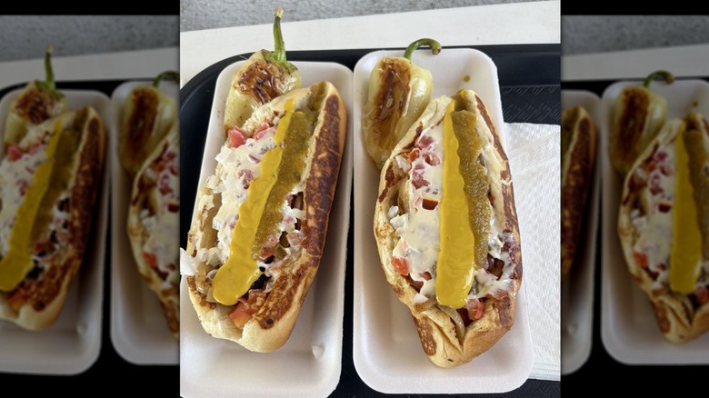 Two hot dogs, each in their own white styrofoam container set on a black cafeteria tray