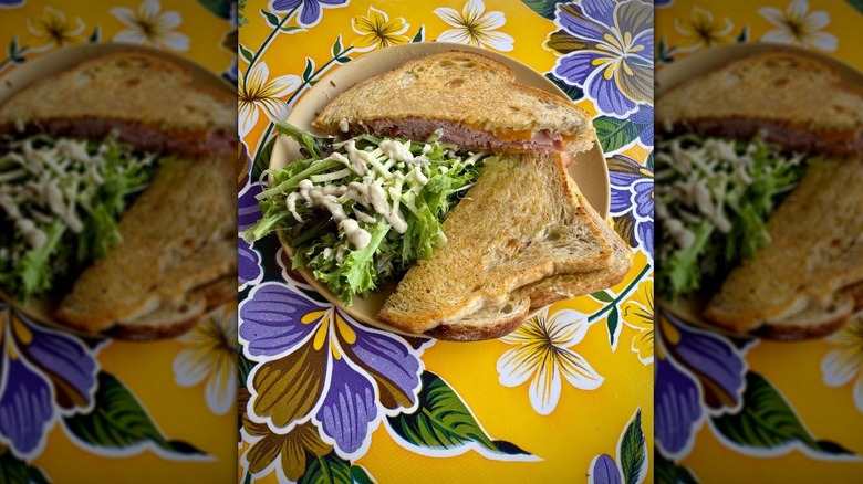 Ham and cheese sandwich on toasted bread and salad on plate on colorful tablecloth