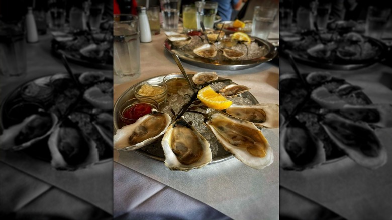 Six half oyster shells garnished with a lemon wedge on an iced round silver platter