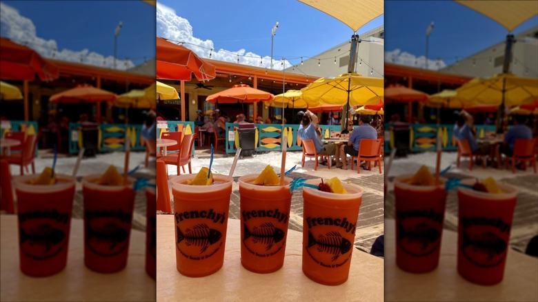 Three red blended drinks, garnished with oranges in clear plastic cups