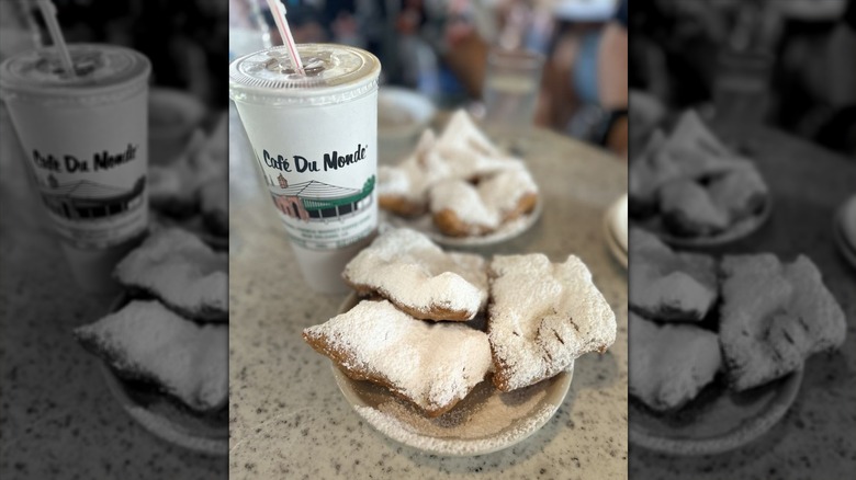 A paper plate with three confectioners' sugar-covered beignets, and drink at Café du Monde