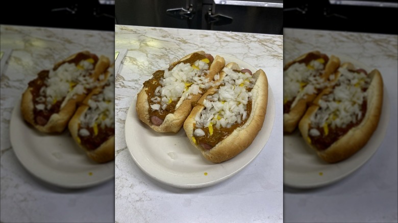 Two hot dogs on a white plate covered in chili, mustard, and chopped onions