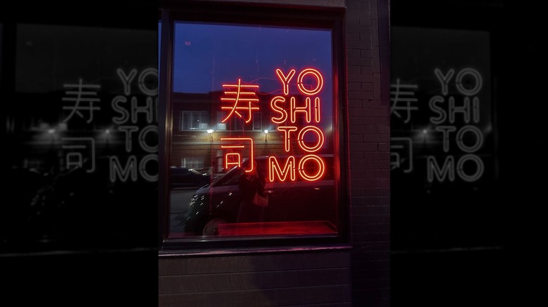 A red neon Yoshimoto sign in a window, lit at night