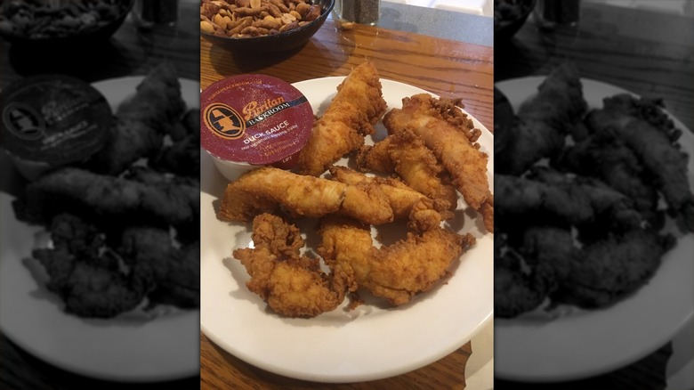A white plate with chicken tenders on it with a pre-packaged container of Puritan's duck sauce