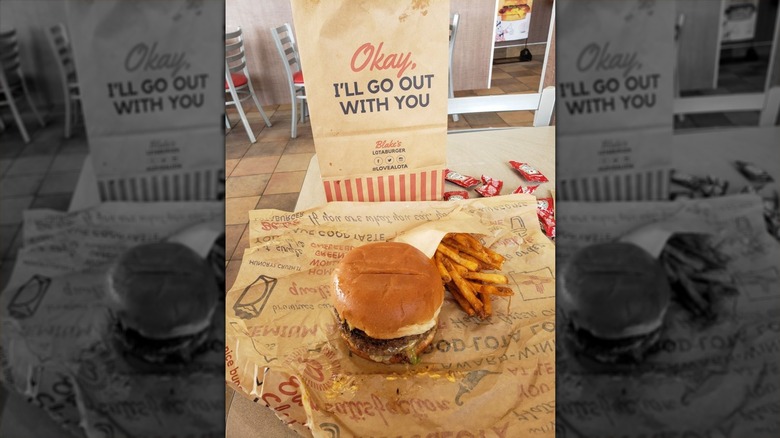 A Blake's Lotaburger burger sitting on its wrapper with an order of fries on the side and a Blake's paper bag in the background