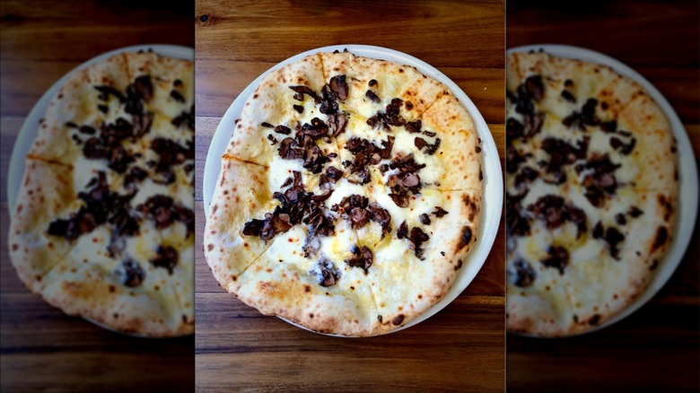 A whole Fireflour mushroom pizza on a white plate on a wood surface