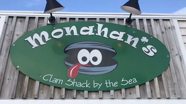 Green Monahan's Clam Shack by the Sea exterior sign featuring a cartoonish clam affixed to gray weathered wood
