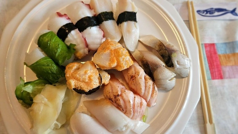 Overshead photo of a white plate filled with assorted sashimi and chopsticks below it