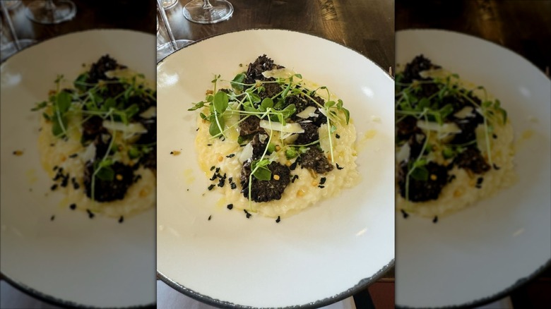 A white plate with risotto on it; topped with chopped mushrooms and greens